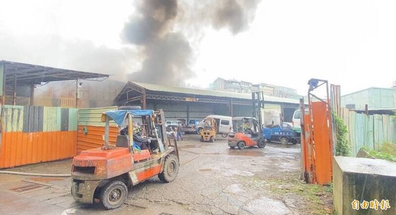 桃园区树仁三街网拍仓库火灾有扩散到后方废车辆与废轮胎回收场之虞，回收场奈及利亚裔张姓男负责人与员工、邻近业者协助，出动多部推高机吊挂废轮胎到场外、移置费车辆到场区另一侧。（记者陈璟民摄）