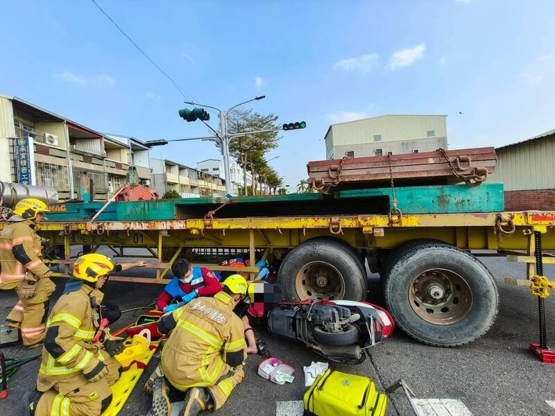 机车与拖板车擦撞后，女骑士卡在轮下，消防队动员抢救。（民众提供）